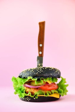 Fast food kavramı. Pembe bir arka plan üzerinde bıçak ile sulu siyah burger. Yemek götürün. Sağlıksız beslenme çerçeve kopya alanı ile.