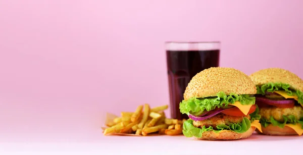 Fast food banner. Juicy meat burgers, french fries potatoes and cola drink on pink background. Take away meal. Unhealthy diet concept with copy space.