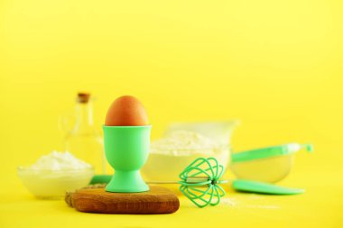 Fırında vakti geldi. Fırın malzemeleri - tereyağı, şeker, un, yumurta, yağ, kaşık, oklava, fırça, çırpma teli, süt Sarı zemin üzerinde. Ekmek yiyecek çerçeve, kavram yemek. Kopya alanı