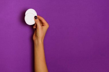 Mor arka planda beyaz pamuk pedi tutan kadın eller. Pankart. Cilt bakımı, saf güzellik, vücut tedavisi konsepti