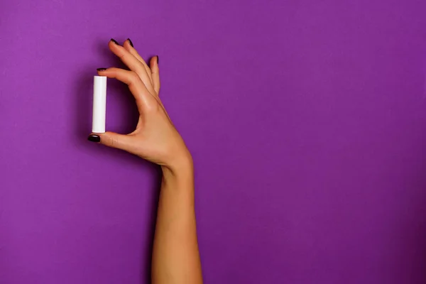 Mains féminines tenant une bouteille cosmétique blanche sur fond violet. Bannière. Soins de la peau, beauté pure, concept de traitement du corps — Photo