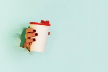 Mavi arka planda beyaz kağıt bardak tutan bir kadın. Kahve fincanı konseptini çıkar. Kopyalama alanı kullan.