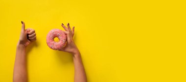 Pembe çöreği tutan kadın ve sarı arka planda 