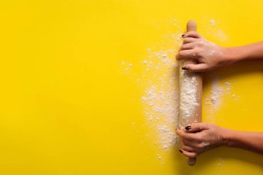 Sarı arka planda un olan kız elleri sürekli yuvarlanıyor. Pasta menüsü, tarif, ev yapımı hamur işi konsepti. Üst Manzara. Metnin için kopyalama alanı olan pankart.