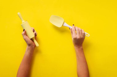 Sarı arka planda mutfak aletlerini tutan kadın. Fırın aletleri, merdane, spatula. Fırın, yemek pişirme, sağlıklı ev yapımı gıda konsepti. Boşluğu kopyala