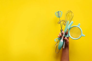 Pişirme düzlüğü. Mutfak aletlerini tutan kadın eller, süzgeç, merdane, sarı arka planda spatula ve bruch. Kopyalama alanı olan pankart.