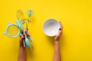 Sarı arka planda mutfak aletlerini tutan kadın. Fırın aletleri - kase, fırça, çırpma, spatula. Fırın, yemek pişirme, sağlıklı ev yapımı gıda konsepti. Boşluğu kopyala.