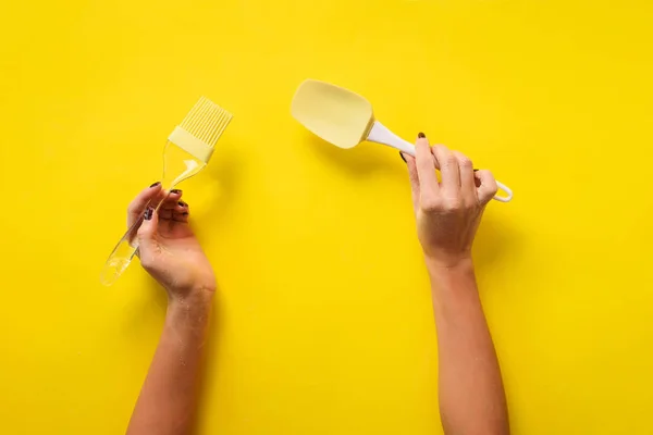 Woman hand holding kitchen utensils on yellow background. Baking tools - brush, whisk, spatula. Bakery, cooking, healthy homemade food concept. Copy space — 스톡 사진