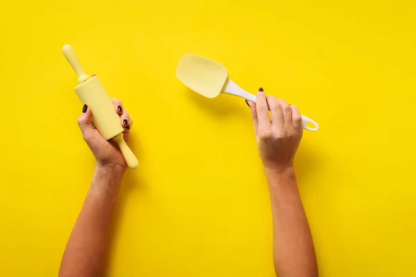 Femme main tenant des ustensiles de cuisine sur fond jaune. Outils de cuisson - rouleau à pâtisserie, spatule. Boulangerie, cuisine, concept d'alimentation maison saine. Espace de copie — Photo