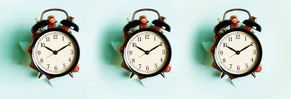 青い紙の背景に穴を通って黒い目覚まし時計を保持する手のシームレスなパターン 警告の概念を起こせ朝のルーティンミニマルスタイルのデザイン — ストック写真