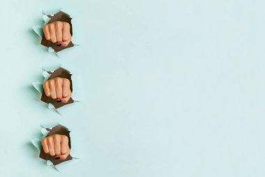 Mavi kağıt arkaplanını delen kadın yumruklarının jeometrik deseni. Savaş, mücadele, çatışma, feminist kavram. Kopyalama alanı olan pankart.