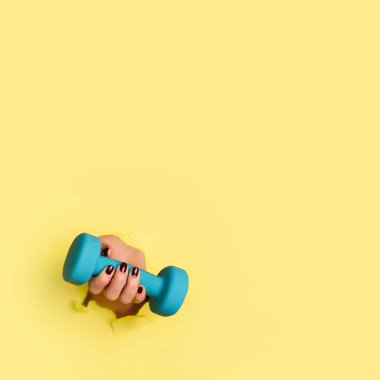 Sarı arka planda mavi dambılı tutan bir kadın. Fitness, spor, sağlıklı yaşam tarzı, diyet konsepti. Fotokopi alanı olan pankart. Kare mahsul.