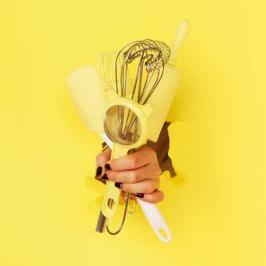 Sarı arka planda mutfak aletlerini tutan kadın. Fırça, çırpma, spatula. Fırın, yemek pişirme, sağlıklı ev yapımı gıda konsepti. Kare mahsul.
