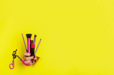 Kadın el ile profesyonel kozmetik araçlar için yapmak: Fırçalar, maskara, ruj, Sarı zemin üzerine kirpik kıvırıcı. Güzellik kavramı. Afiş kozmetik Satılık. Kopya alanı.