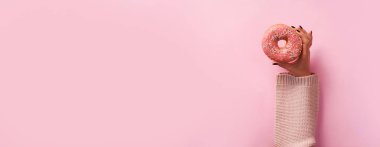 Çörek pembe arka plan üzerinde tutan eller. Üstten Görünüm, düz yatıyordu. Tatlı, tatlı, diyet kavramı. Kopya alanı ile banner. Tatil sonrası kilo.