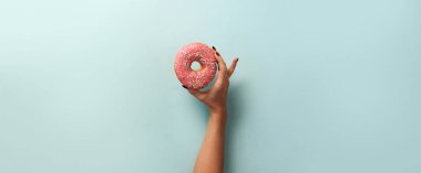 Tatlı çörek mavi arka plan üzerinde tutan el. Üstten Görünüm, düz yatıyordu. Kilo vermişsin, spor, fitness, diyet kavramı. Kopya alanı ile banner