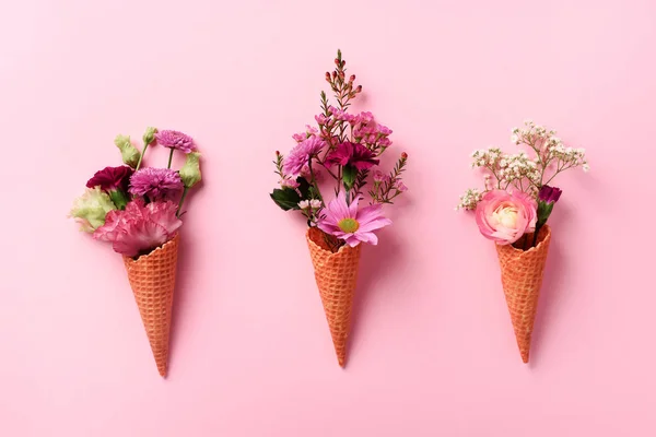 Summer minimal concept. Ice cream cone with pink flowers and leaves on punchy pastel background. Flat lay. Top view. Creative layout.