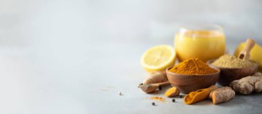 Sağlıklı vegan zerdeçal latte veya altın süt, zerdeçal kök zencefil tozu, siyah biber gri arka plan üzerinde. Ayurvedik tedavi için baharat. Alternatif Tıp kavramı. Kopya alanı ile banner.