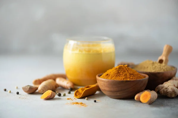 Sağlıklı vegan zerdeçal latte veya altın süt, zerdeçal kök zencefil tozu, siyah biber gri beton arka plan üzerinde. Ayurvedik tedavi için baharat. Alternatif Tıp kavramı.
