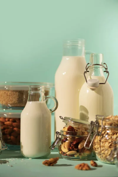 Glass bottles of vegan plant milk and almonds, nuts, coconut, hemp seed milk on blue background. Banner with copy space. Dairy free milk substitute drinks and ingredients.