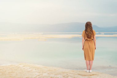 Sarı saçlı parlayan ile genç kız deniz kenarına, Dead Sea beach gider. Afiş. Seyahat, yaz tatili, tatil, özgürlük kavramı. Dijital detoks. Deniz arka plan, kopya alanı