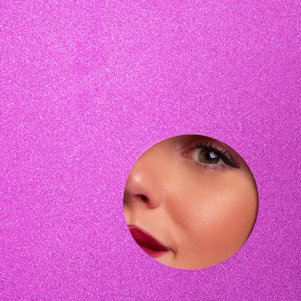 Girl with bright eyes make up looks through hole in violet paper. Business card of artist, beauty concept. Square crop. Cosmetics sale. Beauty salon advertising banner with copy space.
