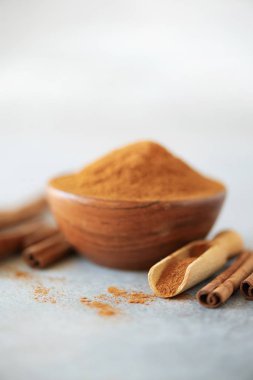 Üzerinde tarçın tozu ve tarçın çubukları olan ahşap bir kâse. Arka planda gri beton ve fotokopi alanı var. Ayurvedik tedavi için baharatlar. Alternatif tıp konsepti.