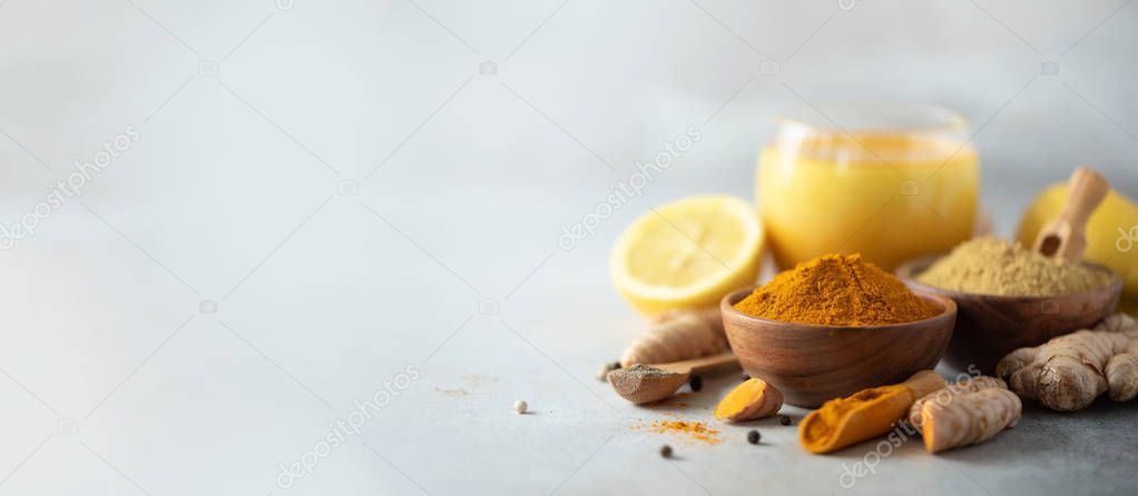 Healthy vegan turmeric latte or golden milk, turmeric root, ginger powder, black pepper over grey background. Spices for ayurvedic treatment. Alternative medicine concept. Banner with copy space