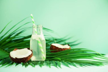 Hindistan cevizi suyu ve taze olgunlaşmış meyve mavi zemin üzerine bir şişe. Yaz gıda kavramı. Vejetaryen, vegan, detoks içecek. Hindistan cevizi suyu ile saman üstünde palmiye yaprakları