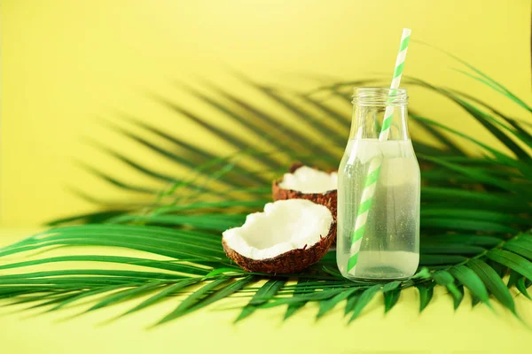 코코넛 물, 노란 배경에 신선한 익은 과일의 병. 여름 음식 개념입니다. 채식, 채식주의 해독 음료 손바닥에 짚으로 코코넛 주스 나뭇잎 — 스톡 사진