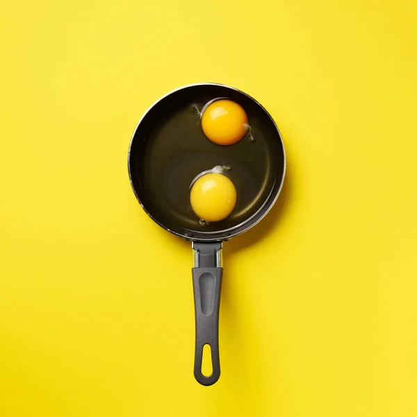 Food concept with two eggs, pan on yellow background. Top view. Creative pattern in minimal style. Flat lay. Square crop — 스톡 사진