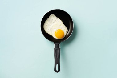 Mavi arka planda tavada pişmiş yumurta ile yaratıcı gıda konsepti. Üst Manzara. Asgari tarzda yaratıcı bir model. Düz yatıyordu