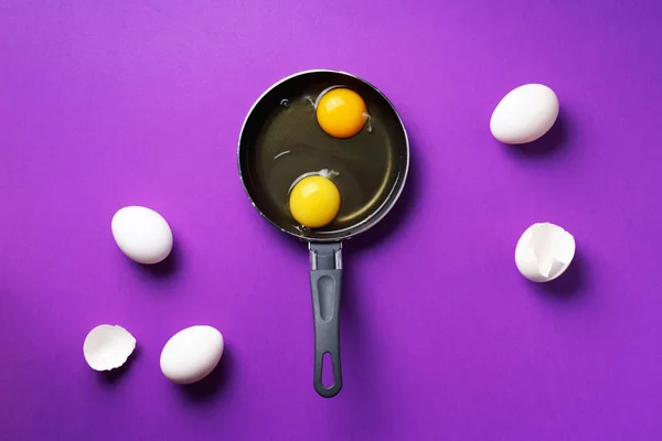 Food concept με δύο αυγά, κελύφη, τηγάνι σε βιολετί φόντο. Στο πάνω μέρος. Δημιουργικό μοτίβο σε minimal στυλ. Επίπεδη. — Φωτογραφία Αρχείου