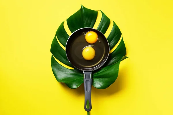 Organic egg in pan over monstera leaf on yellow background. Minimalistic food concept. Top view. Creative layout — 스톡 사진