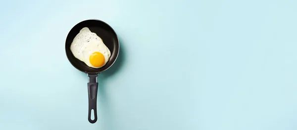 Creative food concept with fried egg on pan over blue background. Top view. Creative pattern in minimal style. Flat lay. Banner — 스톡 사진