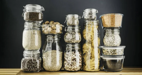 Assortment of uncooked grains, cereals and pasta in glass jars on wooden table. Healthy cooking, clean eating, zero waste concept. Balanced dieting food — Stock Photo, Image