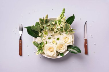 Tabakta beyaz çiçekler, çatal, gri arka planda bıçak. Sağlıklı beslenme, vejetaryen diyeti. Yaratıcı düzen. Üst manzara, düz uzanma