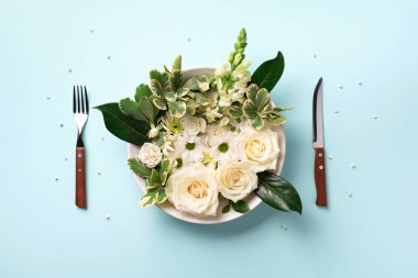 Tabakta beyaz çiçekler, çatal, pastel mavi arka planda bıçak. Sağlıklı beslenme, vejetaryen diyeti. Yaratıcı düzen. Üst manzara, düz uzanma