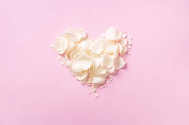 Kalp, pastel pembe arka planda beyaz gül yapraklarından yapılmış. Üst manzara, düz yatış. Aşk ve romantik konsept. Metnin için boşluk kopyala.