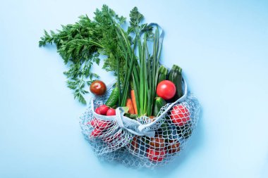Mavi arka planda organik yeşil sebzeli çevre dostu ağ torbası. Düz yerde, üst tarafta. Sıfır atık, plastiksiz konsept. Sağlıklı beslenme ve detoks.