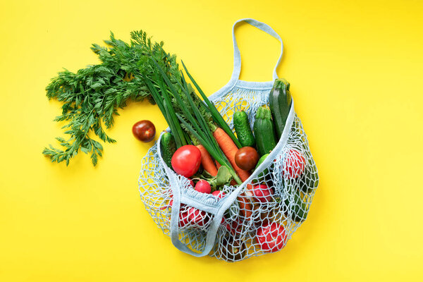 Eco friendly mesh bag with organic green vegetables on yellow paper background. Flat lay, top view. Zero waste, plastic free concept. Healthy clean eating diet and detox.