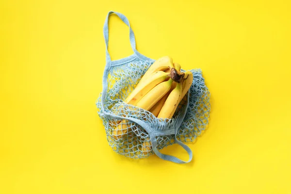 Banano orgánico en bolsa de malla de hilo sobre fondo de papel amarillo. Asiento plano, vista superior. Cero residuos, concepto libre de plástico. Alimentación sana y limpia dieta y desintoxicación. Comida de verano — Foto de Stock