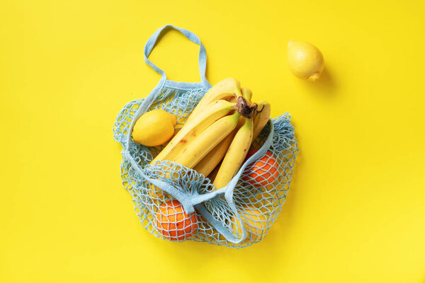 Mesh shopping bag with organic banana, orange, lemons on yellow paper background. Flat lay, top view. Zero waste, plastic free concept. Healthy clean eating diet and detox. Summer fruits