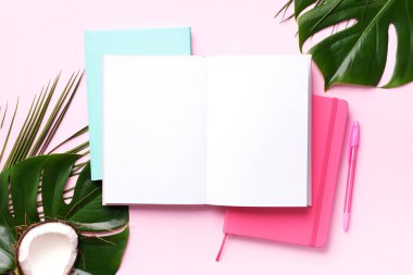Yeşil canavar, palmiye yaprakları, hindistan cevizi, pembe arka planda not defterleri. Kadın blog yazarı çalışma alanı kavramı. Düz yatıyordu. Üst görünüm.