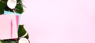 Kadın blog yazarı çalışma alanı kavramı. Yeşil canavar palmiye yaprakları, pembe arka planda hindistan cevizi ve fotokopi alanı. Pankart. Düz yatış, üst görünüm.