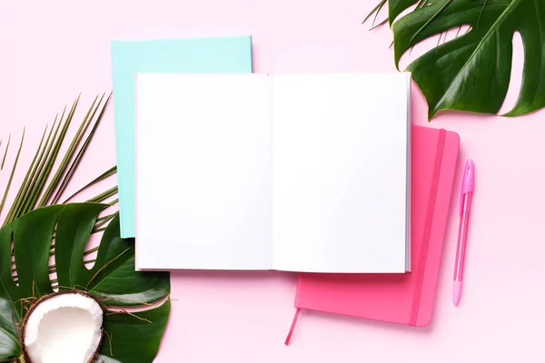 Monstera verde, folhas de palma, coco, cadernos sobre fundo rosa. Feminino conceito de espaço de trabalho escritor blog. Deitado. Vista superior . — Fotografia de Stock