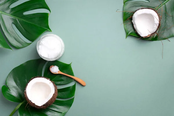 Kokosöl und reife Kokosnüsse, tropische Palmen- und Monsterblätter auf grünem Hintergrund mit Kopierraum. Ansicht von oben. Kreative Gestaltung im Sommer. — Stockfoto