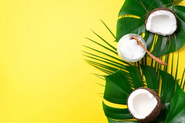 Kokosöl und reife Kokosnüsse, tropische Palmen- und Monsterblätter auf gelbem Hintergrund mit Kopierraum. Ansicht von oben. Kreative Gestaltung im Sommer. — Stockfoto