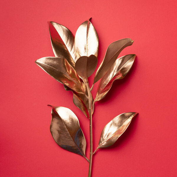 Floral minimal style concept. Exotic summer trend. Golden tropical leaves and branch on red color background. Shiny and sparkle design, fashion concept.
