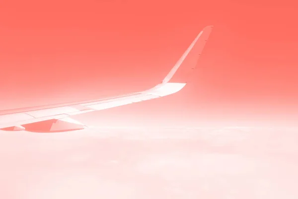 Travel concept. Wing of airplane flying above the clouds in trendy coral sky. Copy space — Stock Photo, Image